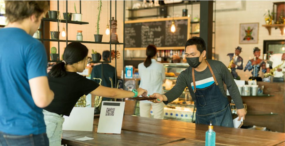 A worker at a small business wearing a mask helps a customer pay for services | The Fate of Small Business in Metro Vancouver