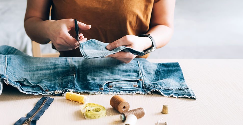 A woman repairs a pair of jeans on a table surrounded my fabric materials. The Case for Circular Fashion and Apparel in Vancouver