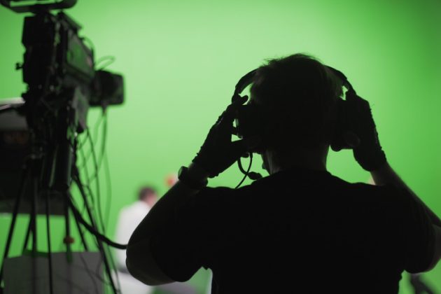 A film director in on a green screen film set adjusts his headphones. Vancouver film industry update.