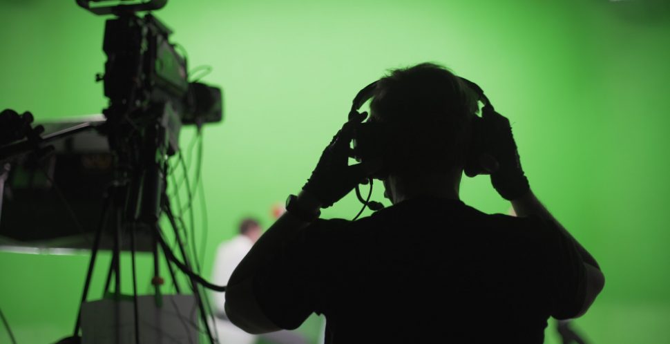 A film director in on a green screen film set adjusts his headphones. Vancouver film industry update.